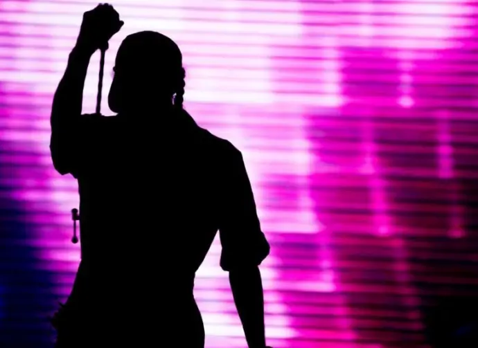 Silhouette of an artist singing live on the stage in the front of a colorful background