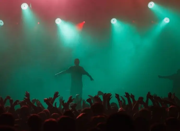 Rap singer performing on concert in music hall. Silhouette of rapper singing on stage in night club. Popuar hip hop music festival. Crowd of fans partying on dance floor
