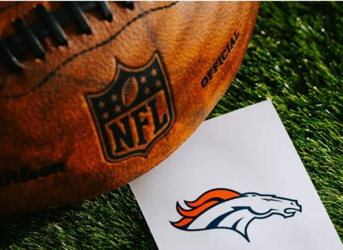 Denver Broncos NFL team Logo and American football ball on Green Grass.