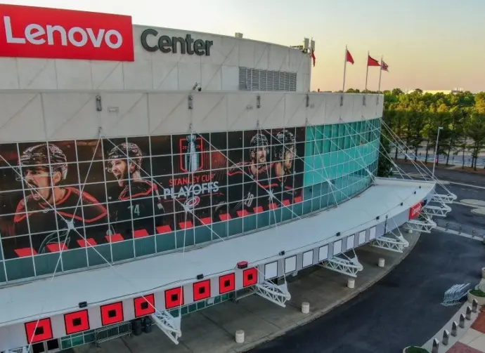 Low angle^ architectural detail shot looking up at the front entrance of the Lenovo Center. The glass facade of the arena is covered in large-scale promotional branding for the 2026 Stanley Cup Playoffs Eastern Conference Finals matchup between the Carolina Hurricanes and Montreal Canadiens. Prominent window vinyls feature portraits of team captain Jordan Staal and alternate captains Sebastian Aho and Jaccob Slavin alongside corporate venue logos^ captured under clear evening conditions ahead of the playoff series in North Carolina. Raleigh^ NC^ USA - May 19^ 2026