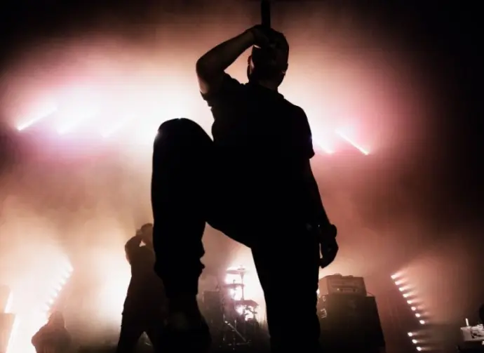 A dark silhouette of a singer on the stage. Good-looking background^ bright stag lights. A concert of a famous music band