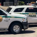 Two Miami-Dade police K-9 cars are parked near a metal security fence on a bright sunny day. Miami^ Florida^ USA^ June 16th 2025