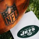 New York Jets logo on the ground and official NFL ball on green grass. Jets card^ edit space