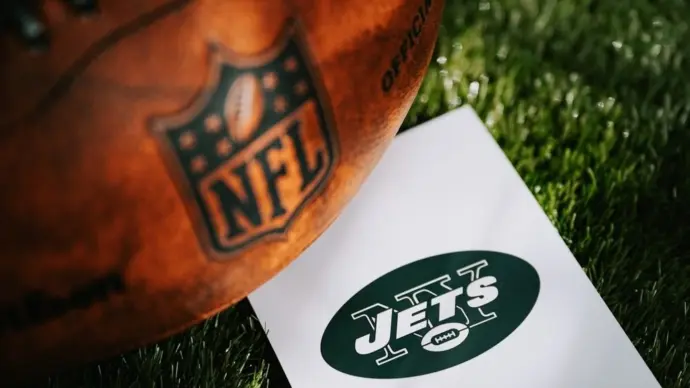 New York Jets logo on the ground and official NFL ball on green grass. Jets card^ edit space