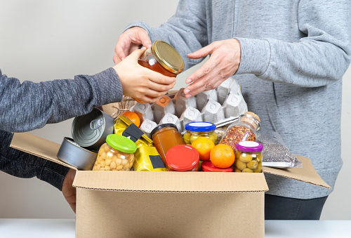 volunteers-hands-putting-grocery-products-foodstuff-to-food-donations-box