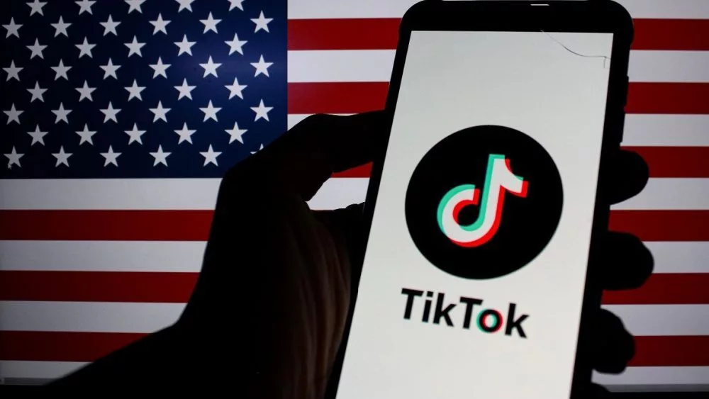 Photo illustration of TikTok logo displayed on a smartphone with American Flag in the background.