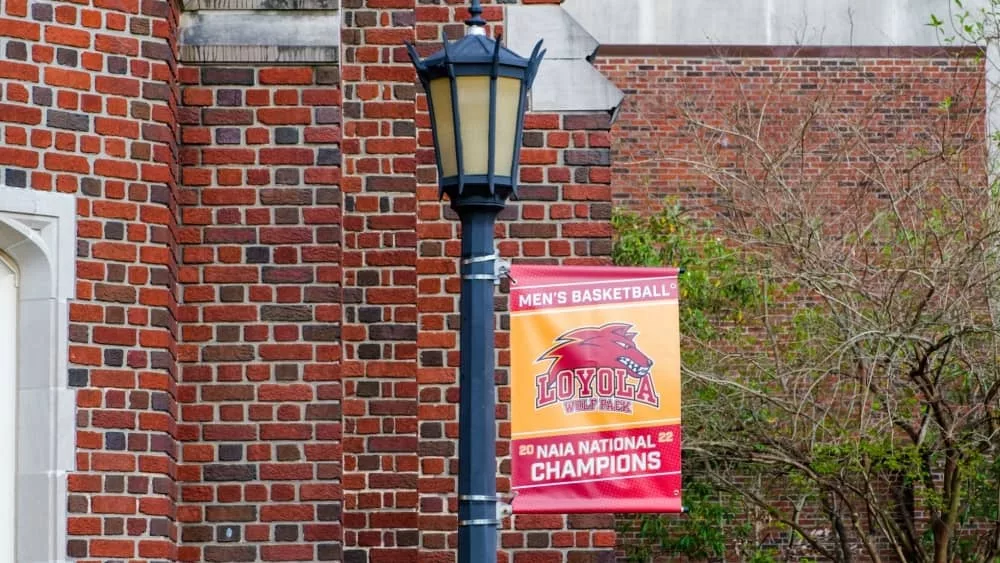 "2022 NAIA Men's Basketball National Champions" banner hangs from lamp post at Louise C. Thomas Hall at Loyola University