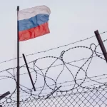 View of russian flag behind barbed wire against cloudy sky. Concept anti-Russian sanctions. A border post on the border of Russia. cancel culture Russia in the world
