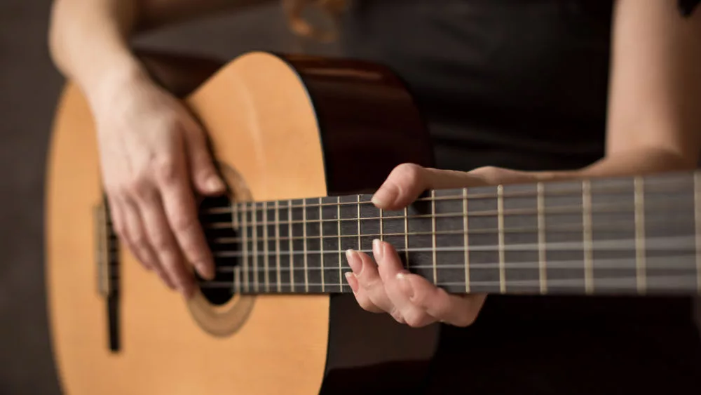 female musician playing guitar^ focus on hands/strings