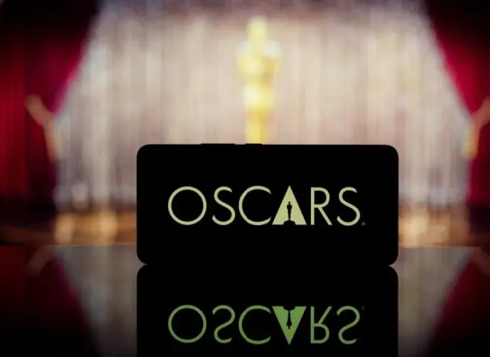 A smartphone displaying the Oscars logo against a blurred awards ceremony background. January 13^ 2025