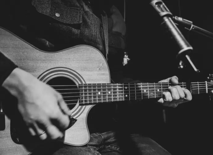 The guitarist plays an acoustic guitar with a capo in front of a microphone. The concept of music recording^ rehearsal or live performance.
