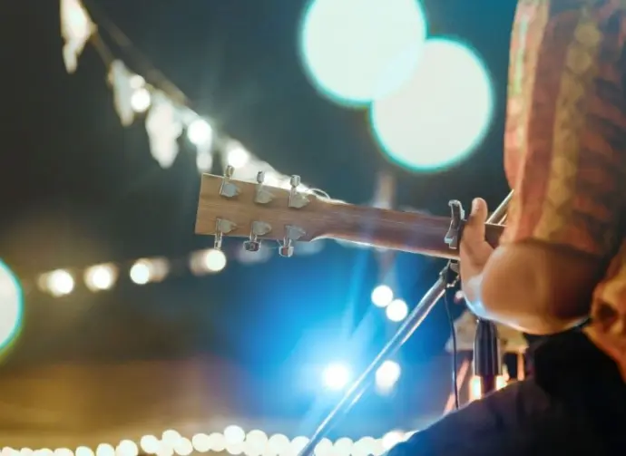 Musical and enjoyment concepts. Rear view of the man sitting play acoustic guitar on the outdoor concert with a microphone stand in the front.