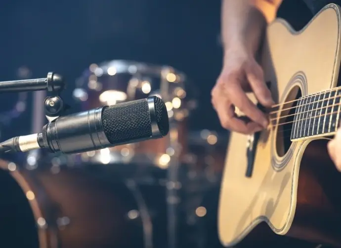 Male musician playing acoustic guitar behind microphone in recording studio.
