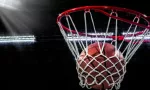 Looking up at an orange basketball falling through the rim and a white nylon net. With the arena lights in the background.