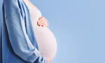 pregnant woman holding her belly in silhouette/ blue background.