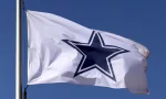 Dallas Cowboys flag flies in front of the AT&T Stadium located in Arlington^ Texas on March 14^ 2014. AT&T Stadium is home to the Dallas Cowboys of the NFL.