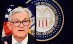 Federal Reserve (Fed) Chair Jerome Powell is visible on smartphone screen. In the background^ an inflation rate chart is displayed.