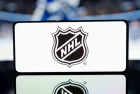 A smartphone displaying the NHL logo with a blurred hockey game in the background. January 13^ 2025