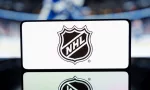 A smartphone displaying the NHL logo with a blurred hockey game in the background. January 13^ 2025