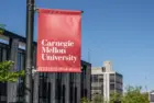Carnegie Mellon University campus entrance sign with buildings in the background. Pittsburgh^ Pennsylvania^ USA- May 13^ 2021: Carnegie Mellon University campus entrance sign with buildings in the background. CMU is a private research university