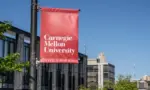 Carnegie Mellon University campus entrance sign with buildings in the background. Pittsburgh^ Pennsylvania^ USA- May 13^ 2021: Carnegie Mellon University campus entrance sign with buildings in the background. CMU is a private research university