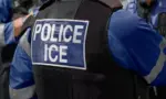ICE police agent - Officer of Immigration and Customs Enforcement. Close-up of POLICE ICE marking on the back of a stab proof vest uniform worn by a trio of police officers at the scene of an incident