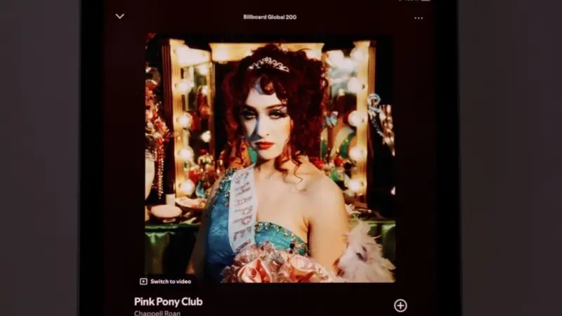 An Apple iPad displays the Spotify music streaming app. The screen the shows the song 