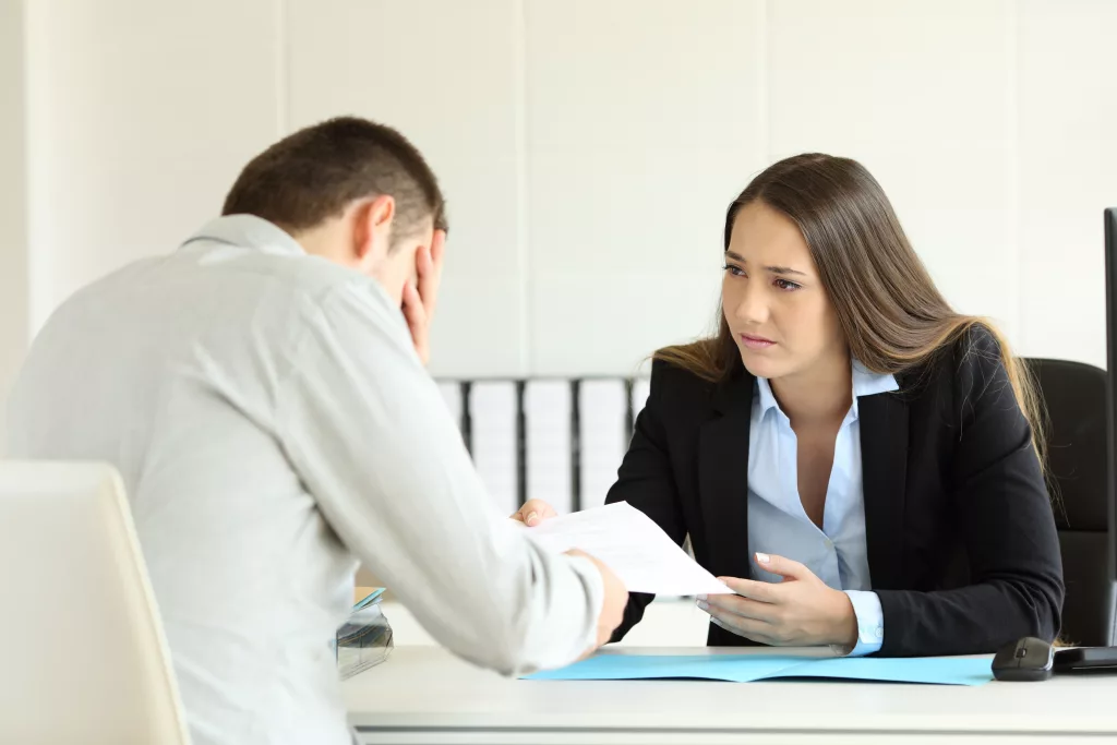sadbossfiringanemployeesittinginherdesktopat