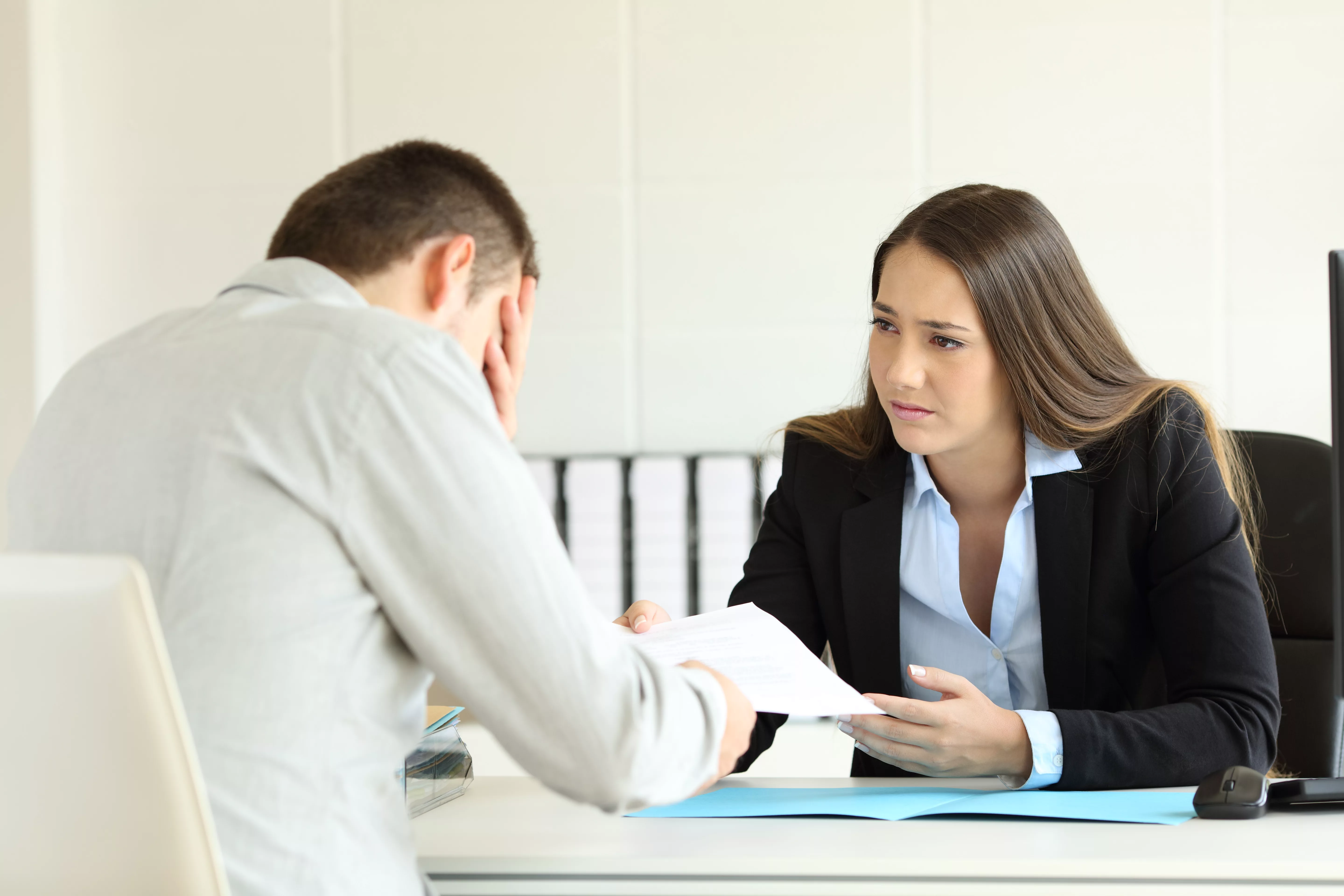 sadbossfiringanemployeesittinginherdesktopat
