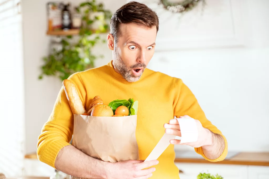 surprisedmanlookingatstorereceiptaftershoppingholdinga