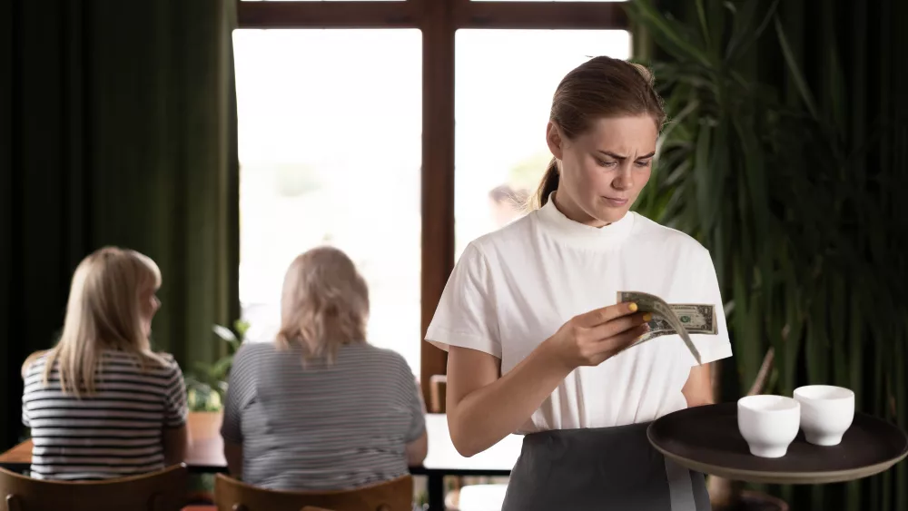 disgruntledfemalewaiterholdingservingtrayinrestaurantwithbad