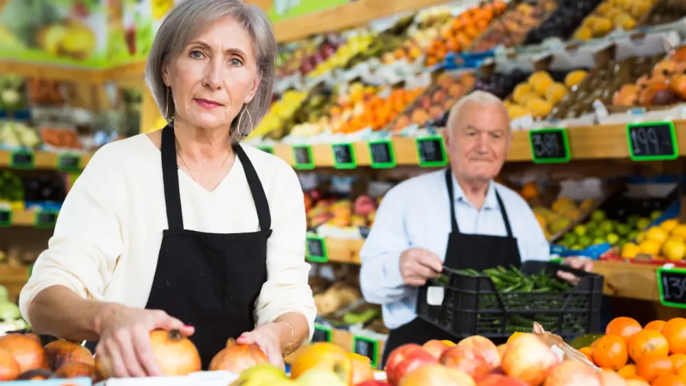 womanmerchandiserinapronputtinggoodsonshelfingreengrocer