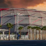 The Intuit Dome with cars driving on the street^ lush green palm trees and powerful clouds at sunset in Inglewood California USA. Inglewood^ California USA - 10 22 2024