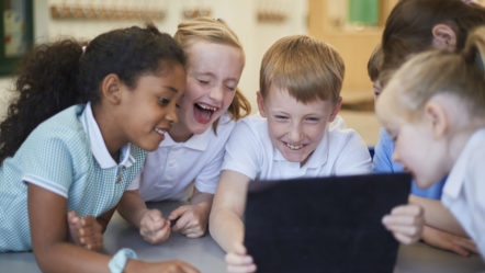 schoolboys-and-girls-laughing-at-digital-tablet-in-classroom-at-primary-school