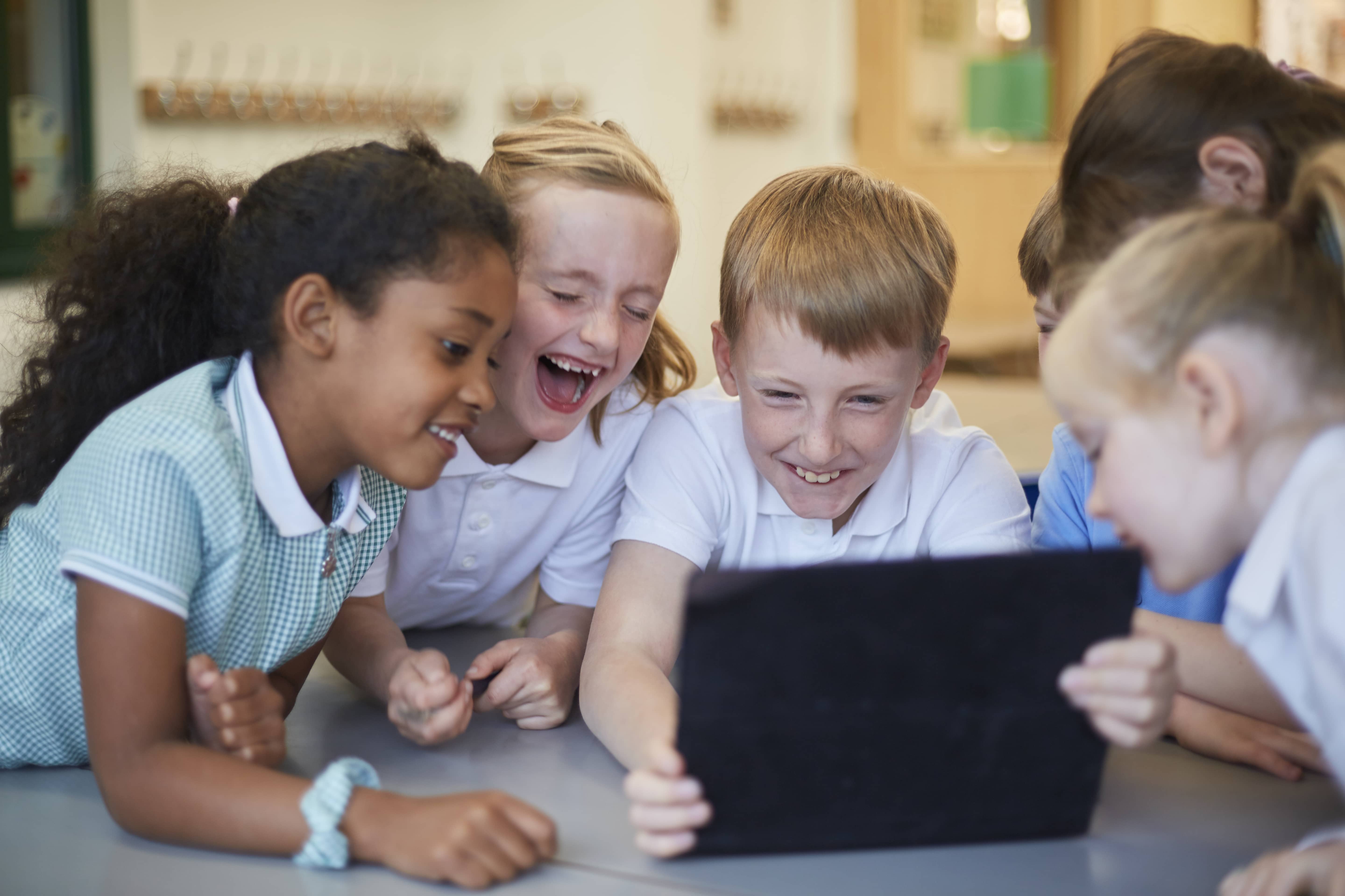 schoolboys-and-girls-laughing-at-digital-tablet-in-classroom-at-primary-school