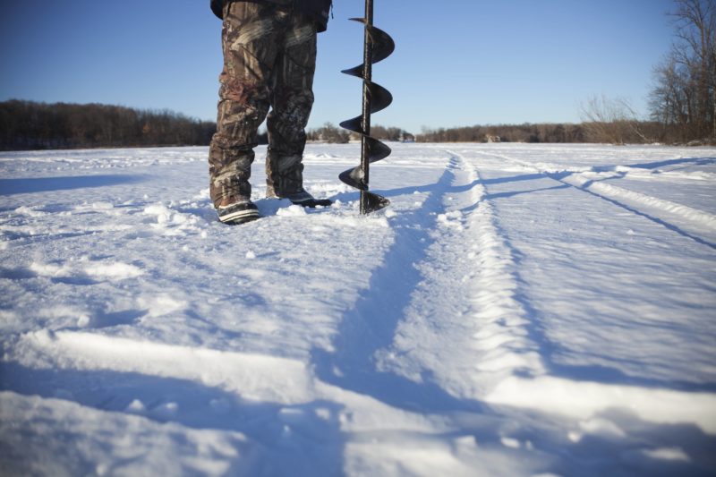 ice-fisherman-drills-hole-with-auger-on-lake-in-minnesota