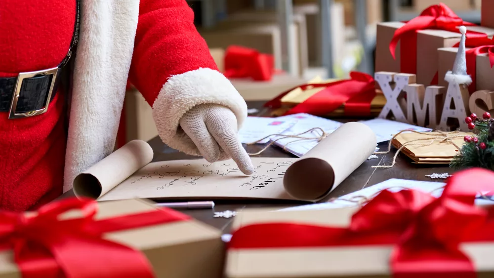 santa-claus-reading-wish-list-standing-at-table-in-workshop-close-up