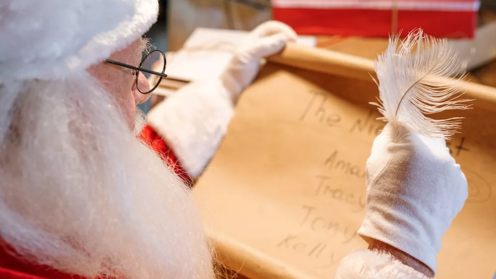 gloved-santa-claus-with-feather-in-hand-looking-through-nice-list