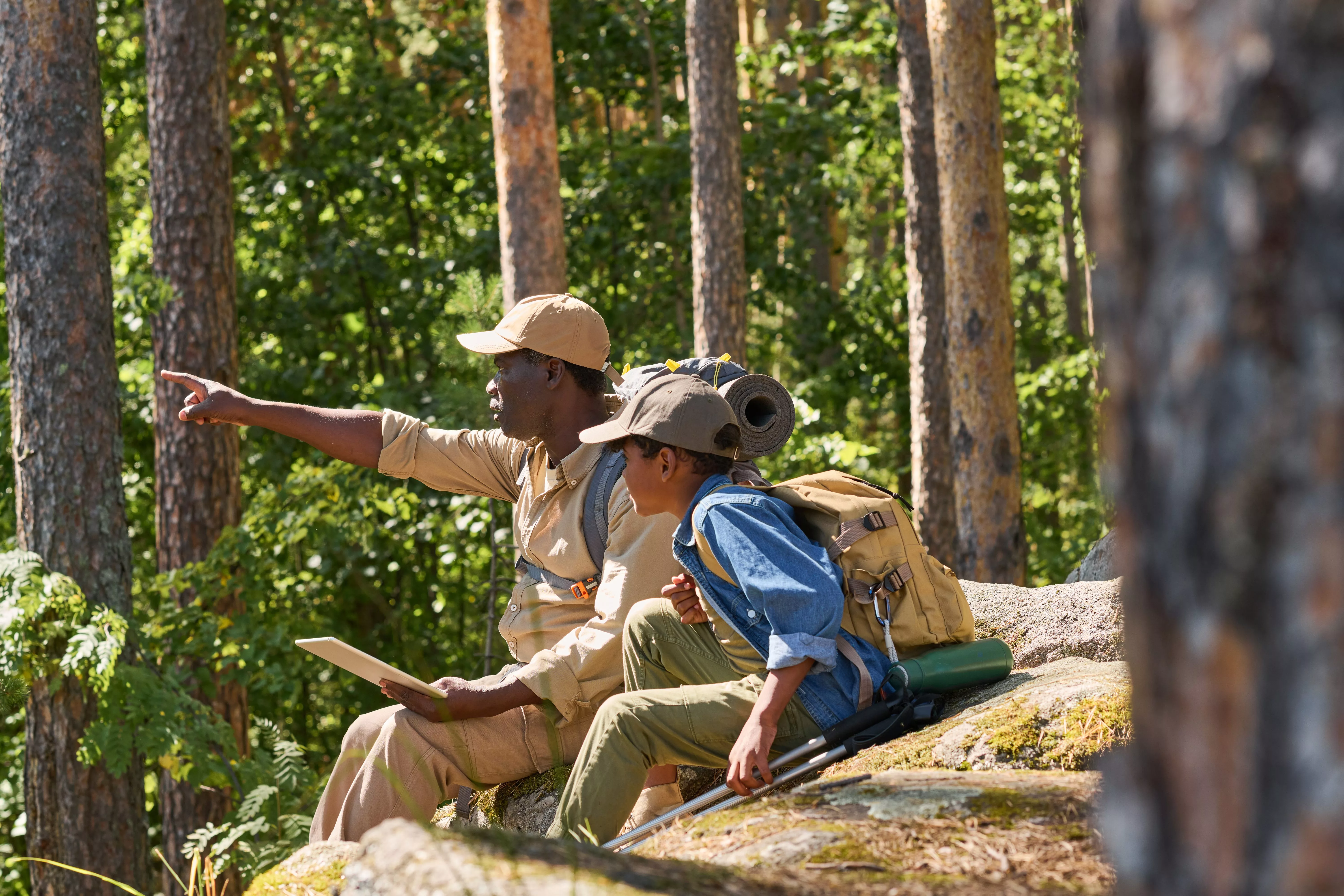 confident-senior-man-pointing-forwards-while-sitting-on-stone-next-to-grandson