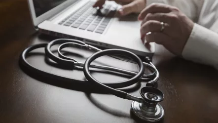 medical-stethoscope-resting-on-desk-as-male-hands-type-on-computer-keyboard