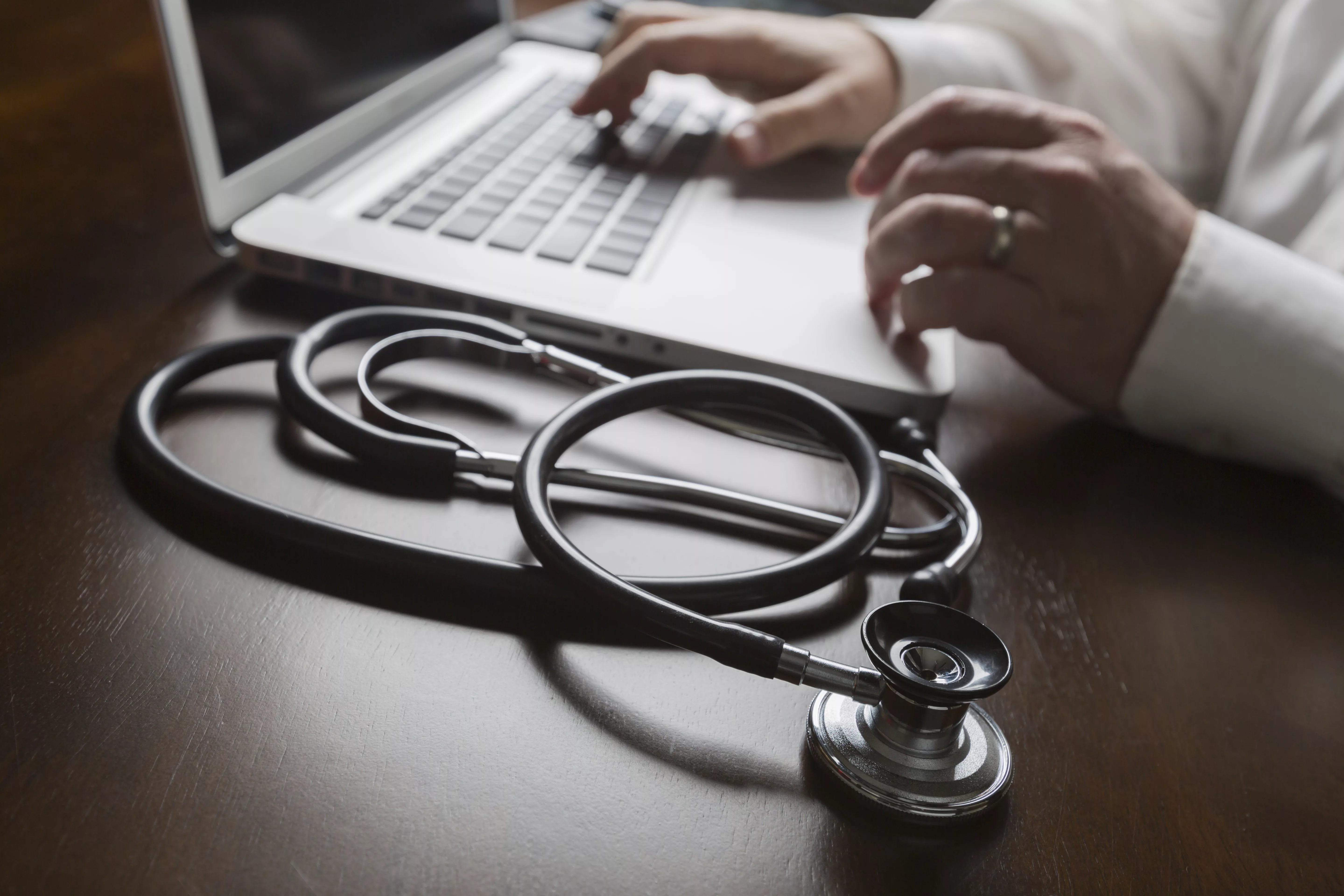 medical-stethoscope-resting-on-desk-as-male-hands-type-on-computer-keyboard