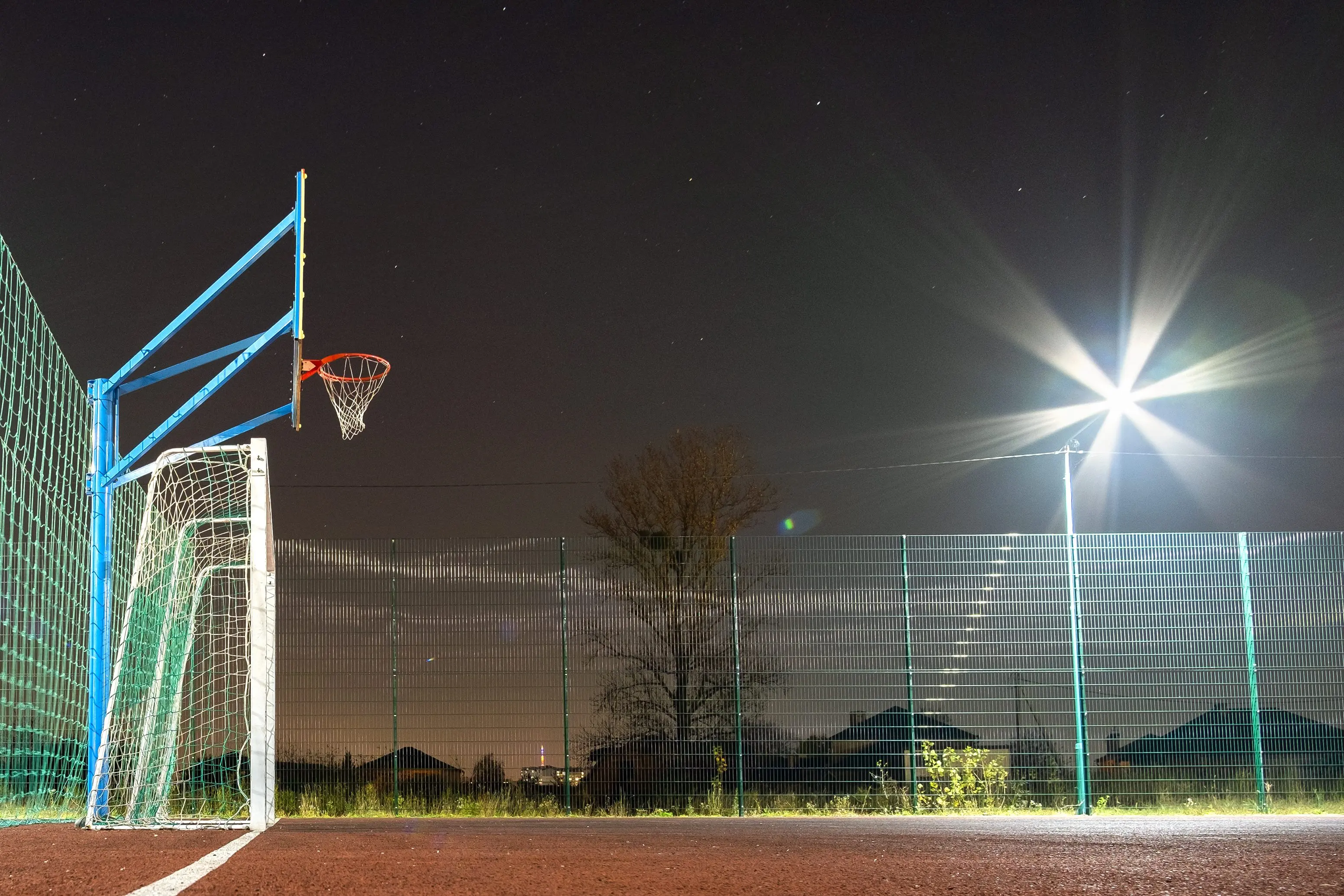 outdoors-mini-football-and-basketball-court-with-ball-gate-and-basket-surrounded-with-high-protective-fence-brightly-illuminated-with-spotlight-lamps-at-night