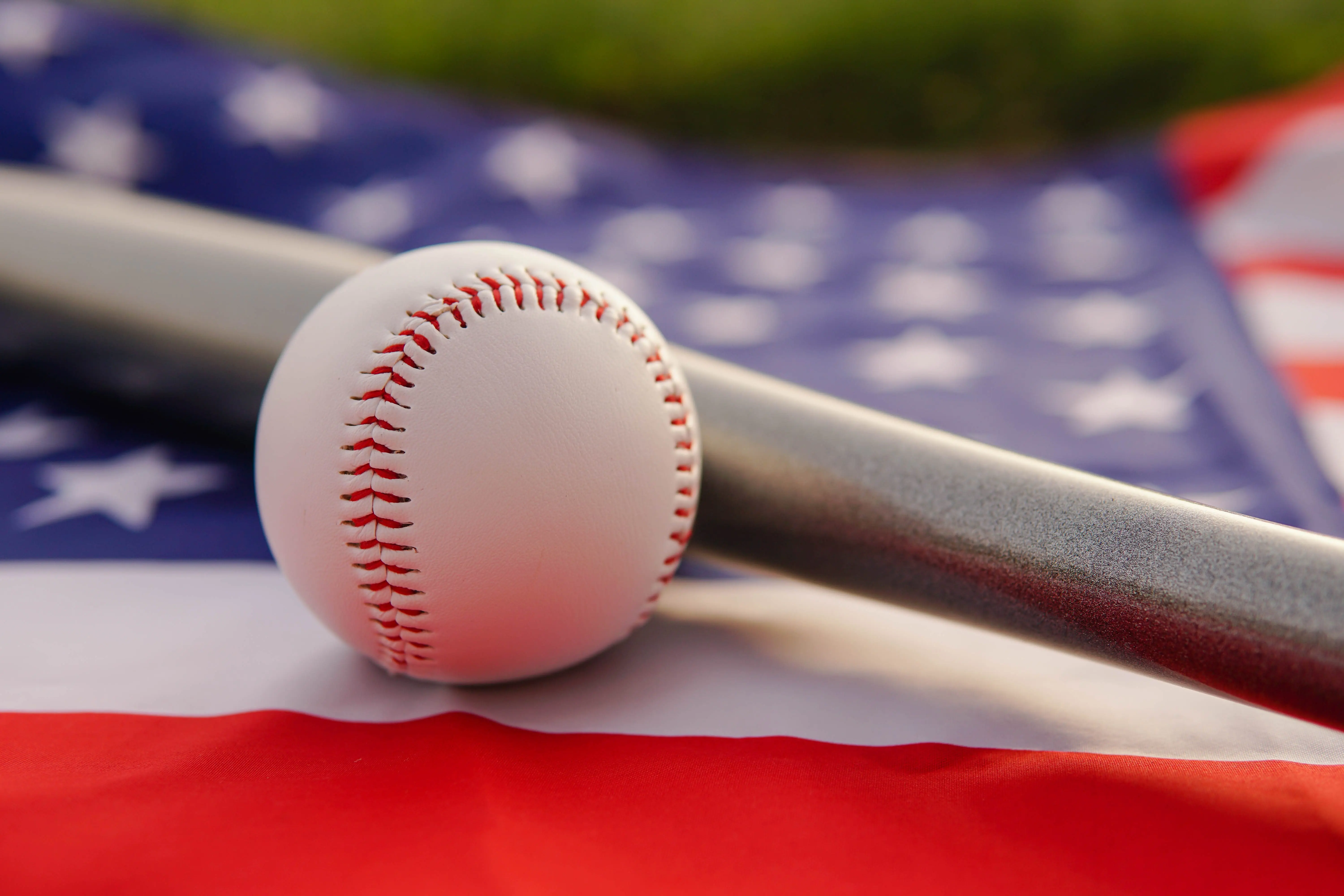 white-leather-ball-and-baseball-bat-laying-on-flag-of-the-united-states-of-america-usa-at-sunset
