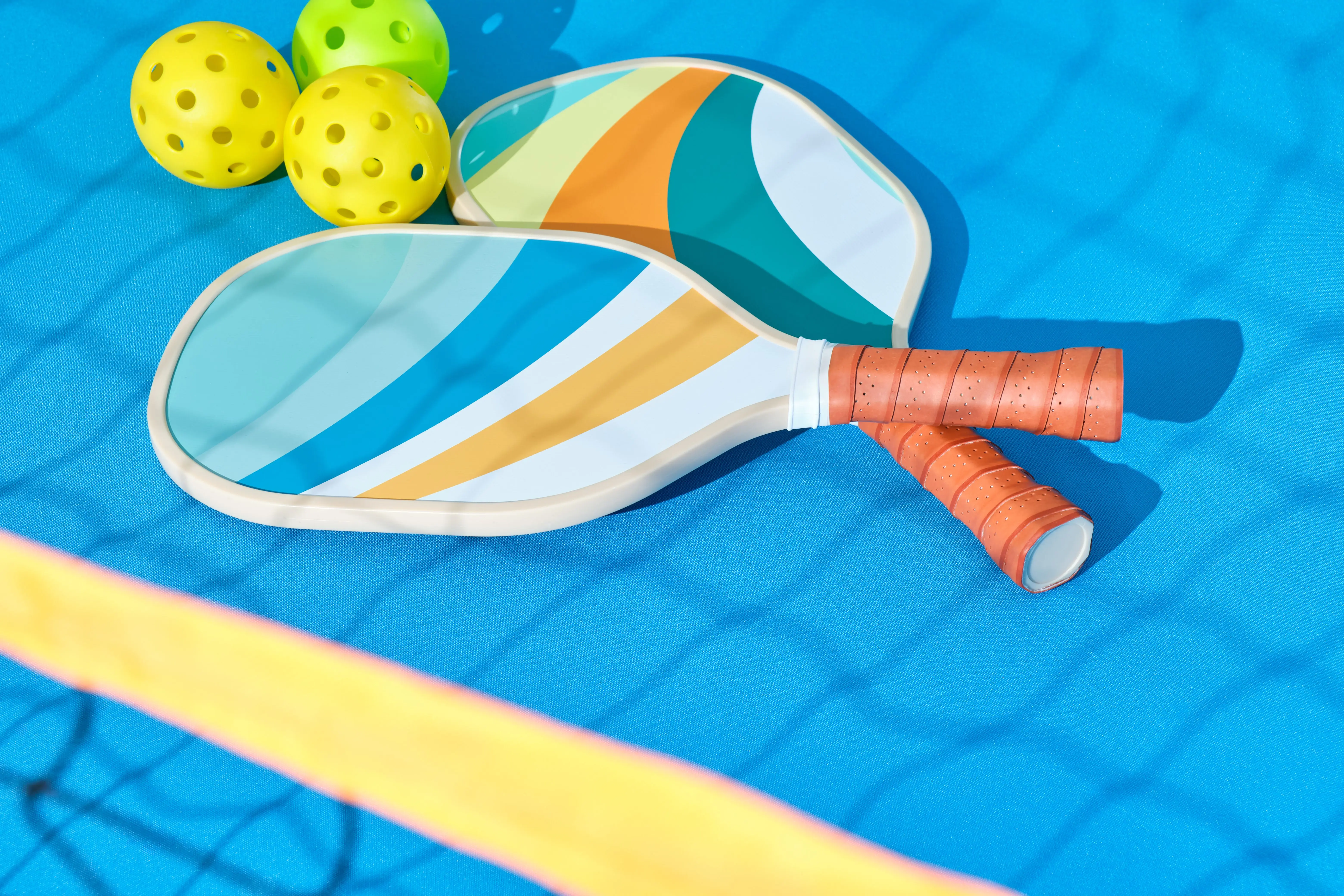 pickleball-paddles-with-balls-to-the-side-with-the-shadow-of-the-net-in-front-on-a-blue-background
