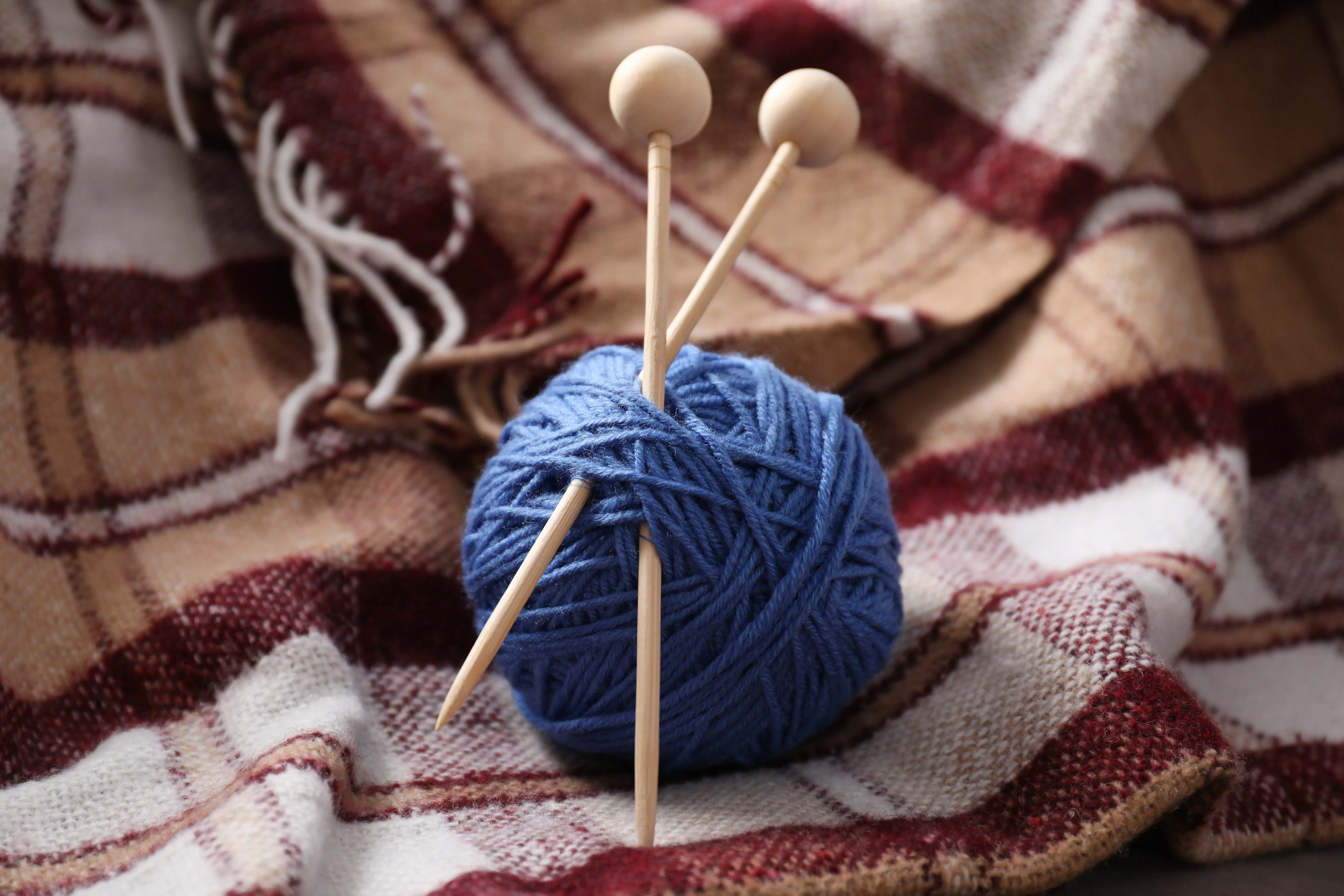 ball-of-yarn-with-knitting-needles-on-checkered-plaid