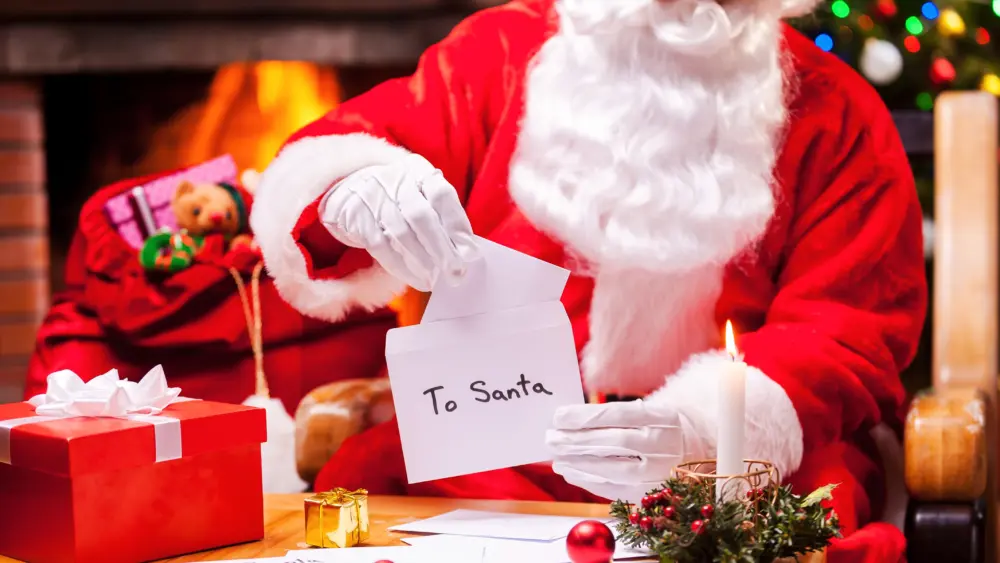 santa-at-work-close-up-of-santa-claus-reading-letters-while-sitting-at-his-chair-with-christmas-tree-an-fireplace-in-the-background