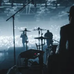 rock band viewed from behind the stage performing to sold-out audience; view of drummers^ guitarists in silhouette in hazy photo