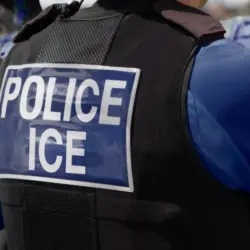 ICE police agent - Officer of Immigration and Customs Enforcement. Close-up of POLICE ICE marking on the back of a stab proof vest uniform worn by a trio of police officers at the scene of an immigrant incident. The ICE federal law enforcement agency is under the supervision of the United States Department of Homeland Security.