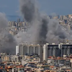 Multiple large plumes of thick grey smoke billow from residential apartment complexes following an explosion or missile strike in a crowded urban skyline. Jan 3 2021 in Iran