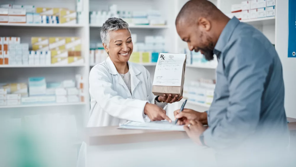 medicine-shopping-or-pharmacist-with-customer-writing-personal-or-medical-information-in-pharmacy-consulting-pills-or-happy-senior-doctor-helping-or-speaking-to-black-man-or-sick-african-customer